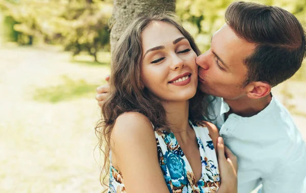 Närbild porträtt av vackra par i kärlek dating utomhus i parken en solig dag. Ung man kysser kind av sin vackra kvinna under picknick utomhus. — Stockfoto