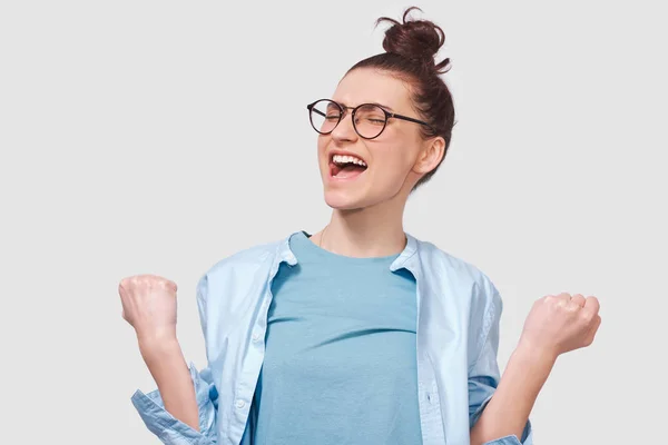 Wesoła młoda kobieta uśmiechnięta szeroko otwartymi ustami, ubierając się w niebieską koszulę, nosząc okrągłe okulary, wyizolowane na białym tle. Koncepcja ludzi i emocji — Zdjęcie stockowe