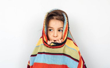 Bir tatil büyük çizgili renkli kazak ile oynarken, gri stüdyo arka plan üzerinde poz, gülümseyen sevimli küçük kız Şaşırttı. Sürpriz çocuk noel zamanında bir hediye için wainting bir kazak dışarı peeks