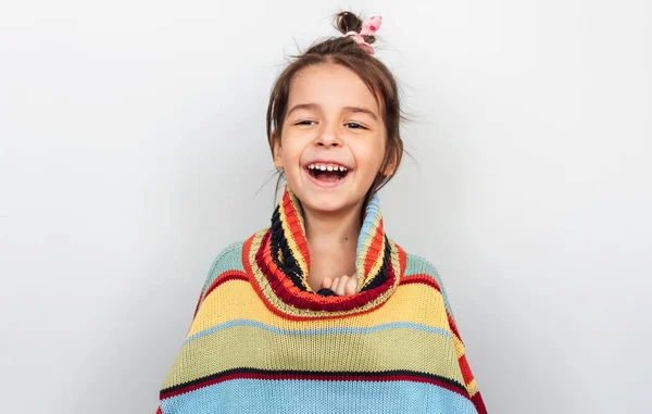 Retrato de uma menina feliz sorrindo e rindo, brincando com grande suéter colorido em um tempo de férias, posando em fundo de estúdio cinza. Criança adorável espreita fora de uma camisola tem emoção positiva . — Fotografia de Stock