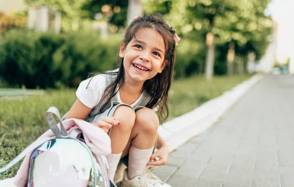 Szabadban portré boldog kislány preschooler mosolyogva nagyjából ül a küszöbön a hátizsák iskola után. Boldog gyermek tanuló pihentető óvoda után. Emberek és oktatási koncepció — Stock Fotó