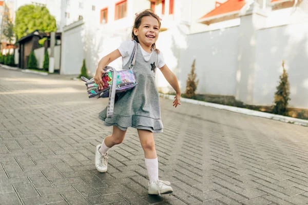 Imagen de la hermosa niña sonriendo, sintiéndose feliz y corriendo con la mochila a su madre después del día de la escuela primaria. Niña alumna caminando en la calle después del jardín de infantes a sus padres. Educación —  Fotos de Stock