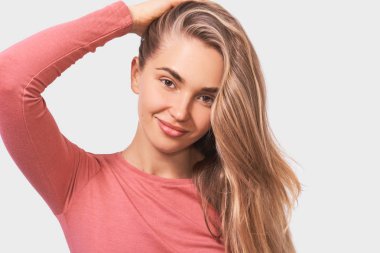 Güzel sağlıklı saçları ile iyi görünümlü genç kadın, olumlu rahat kıyafet giyen ve kameraya bakarak gülümsüyor, beyaz stüdyo duvarında izole. İnsanlar duyguları