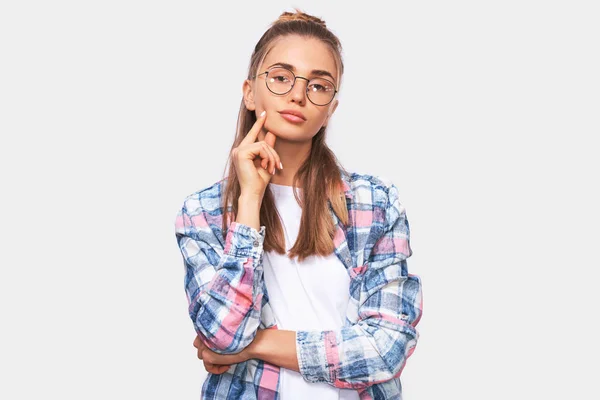 Seriös ung student kvinna tittar på kamera med korsade händer, klädd casual outfit och runda genomskinliga glasögon. Ganska blond kvinna poserar över vit Studio vägg. Människor känslor — Stockfoto