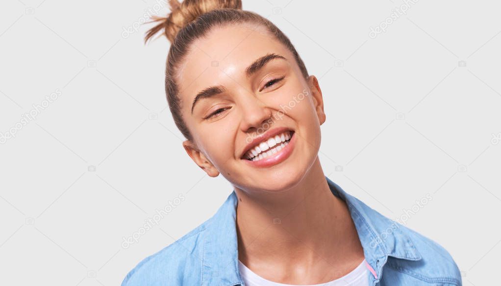 Studio close-up portrait of happy young woman, smiling broadly and positively, wearing casual outfit and looking to the camera, isolated on white background. People and emotions concept