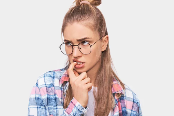 Retrato de cerca de una joven estudiante seria mirando a un lado con el dedo índice en los labios, vistiendo atuendo casual y gafas redondas transparentes. Mujer rubia bonita posando en el estudio . — Foto de Stock