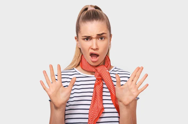 Los gestos de la mujer rubia asombrada se detienen con ambas manos, gritando fuerte, llevando camiseta a rayas y bufanda roja, posando contra la pared blanca del estudio. Mujer confusa diciendo: ¡No!. Personas y emociones —  Fotos de Stock