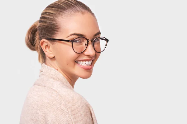 Candid portrait of charming young woman smiling broadly, wearing casual outfit and transparent eyewear, looking to the camera, isolated over white studio background. — Stock Photo, Image