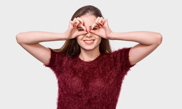 Zadowolony młoda kobieta ubrana w czerwoną koszulę, pokazując OK gesty obiema rękami, udając nosić okulary OT lornetki. Ładna kobieta uśmiechnięta szeroko, stwarzając na białym tle. — Zdjęcie stockowe