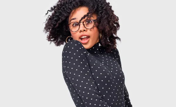 Ritratto di allegra donna afroamericana che sorride e gira con i capelli sani, si sente felice, posa su un muro bianco. Bellissimi capelli afro femminili che soffiano, indossando occhiali trasparenti . — Foto Stock