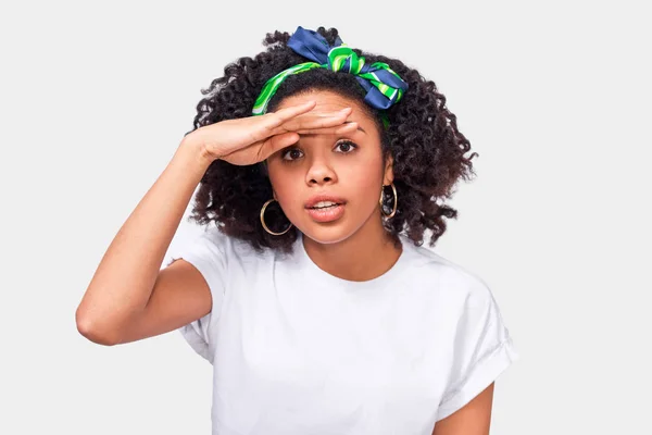 Nahaufnahme Studioporträt einer neugierigen afrikanisch-amerikanischen jungen Frau, die mit der Hand auf der Stirn wegschaut, breit lächelnd, vor weißem Hintergrund stehend. Menschen positive Emotionen Konzept — Stockfoto