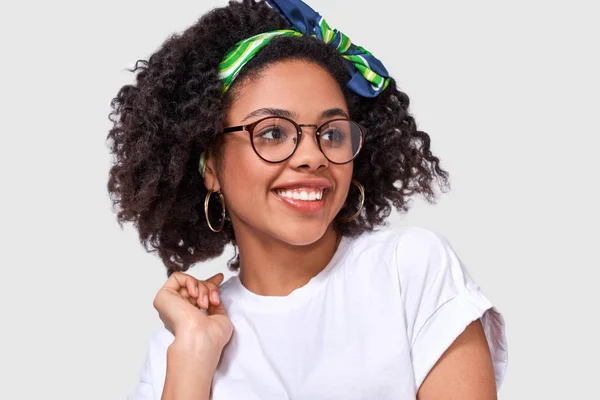 Fröhliche afrikanisch-amerikanische junge Frau mit positivem Lächeln, die zu jemandem beiseite schaut, hat einen freudigen Ausdruck. Charmante dunkelhäutige Frau hat positive Emotionen. — Stockfoto