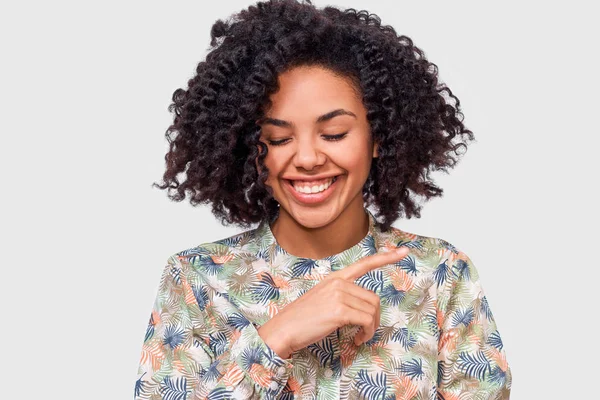 Portrait of gorgeous dark-skinned young woman dressed in floral pattern shirt, feel happy during conversation with a friend. African American female smiling broadly, posing over white wall — Stock Photo, Image
