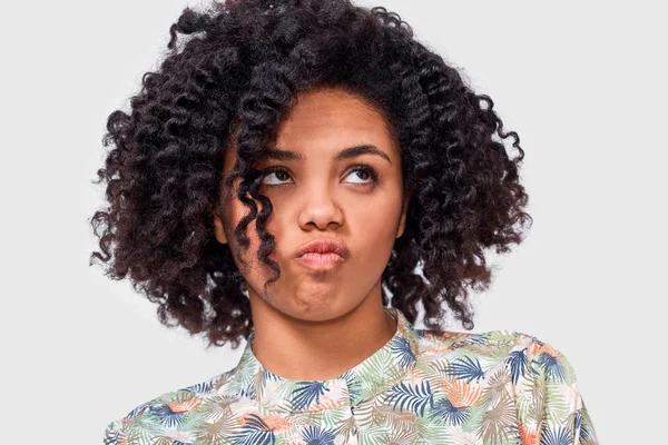 El retrato de cerca de la confundida estudiante afroamericana tiene expresión de dilema, frunce el ceño y mira hacia arriba. Dudosa hembra de piel oscura no puede elegir, aislada en la pared blanca — Foto de Stock