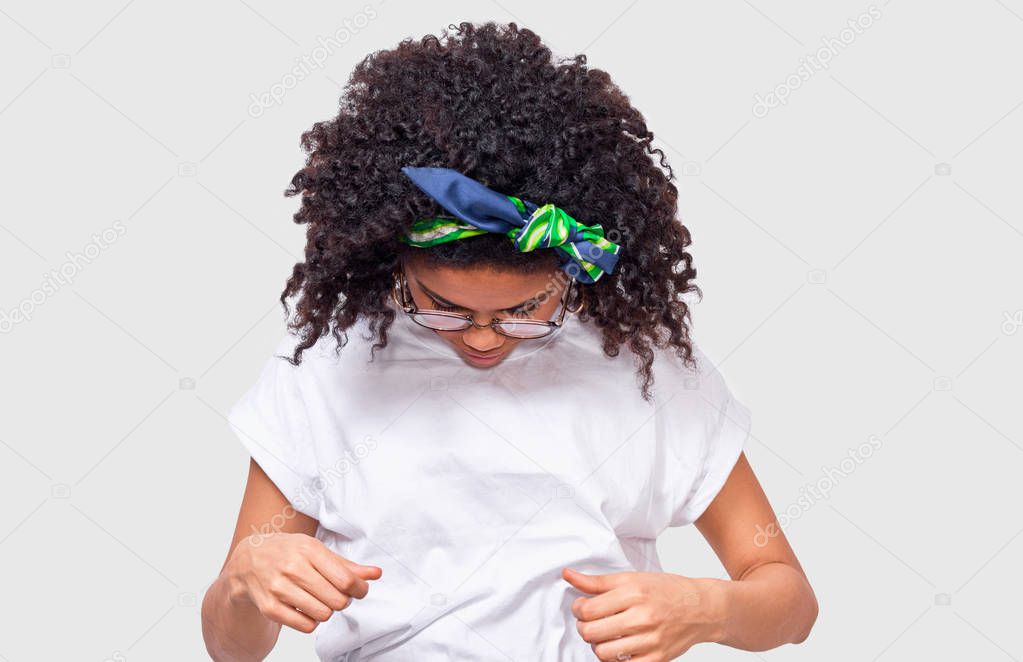 African American young woman looking to her white t-shirt, if it dirty. Afro female wearing cotton t-shirt posing in studio.