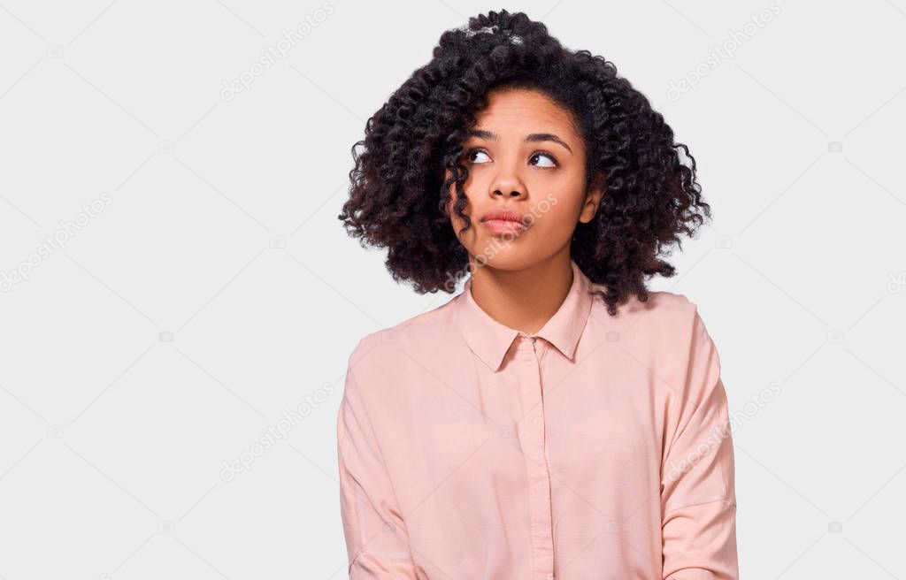 Image of thoughtful African American woman has thinking expression, looking up to the blank copy space. Doubtful dark skinned female can`t make choice, has questioned expression, isolated on white