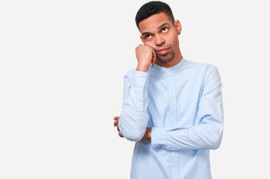 Sıkılmış Afrikalı erkek yandan eğilir, hoş nutuz ifade vardır, rahat mavi gömlek giyen, beyaz stüdyo arka plan karşı duruyor. Çok çalışan Afro-Amerikan adam yorgun hissediyor. İnsanlar ve duygular