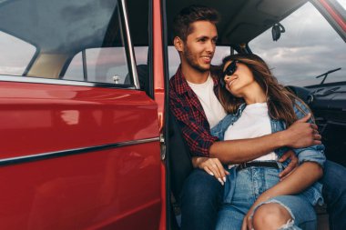 Gün batımı ışığında arabada uzun bir sürücü sonra mutlu romantik genç çift chill Portresi. Yakışıklı genç adam bir yolculuğa güneş gözlüğü takan onun güzel genç kadın tutarak. Yaşam tarzı kavramı.