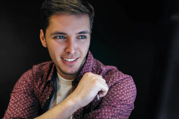 Guapo joven hombre de negocios sonrisa y mirando en el escritorio del ordenador portátil. Fondo negro con espacio de copia. Atractivo gestor masculino planificación y navegación en Internet en el lugar de trabajo. Concepto de estilo de vida . —  Fotos de Stock