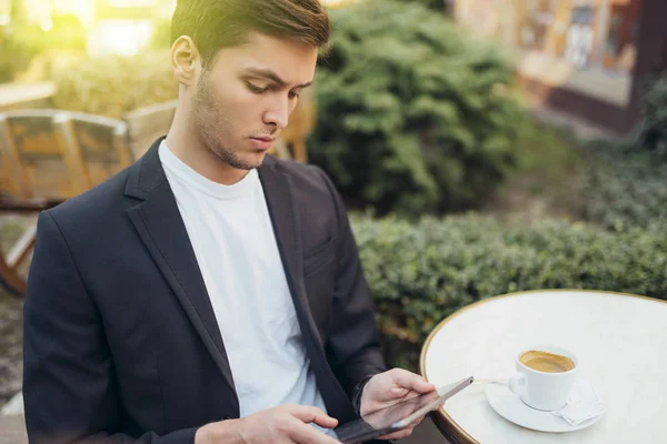 Technology and communication concept. Stylish Caucasian student surfing internet on digital tablet, enjoying free wireless connection at cafe during coffee break. Handsome male messaging online. — Stock Photo, Image