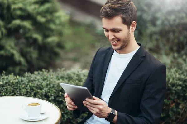 Счастливый кавказский бизнесмен держит планшетное устройство, просматривающее интернет и читающее хорошие новости по электронной почте во время кофе-брейка в современном кафе города. Технологии и бизнес-концепция . — стоковое фото
