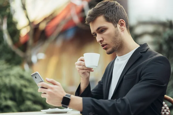 Moderní technika, obchod, komunikace a koncepce lidí. Sebevědomý Kavkazský obchodník s pitím kávy na terase, čtení zpráv z jeho zařízení Smart telefon venku — Stock fotografie