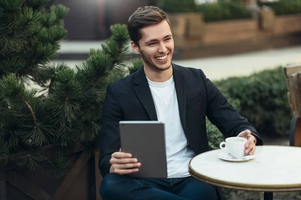 편안한 카페의 테이블에 앉아, 커피를 마시는 디지털 태블릿 컴퓨터에 이메일을 확인하거나 좋은 세계 뉴스를 읽고 캐주얼 착용에 미소 남성의 초상화. 연결 및 기술 개념. — 스톡 사진