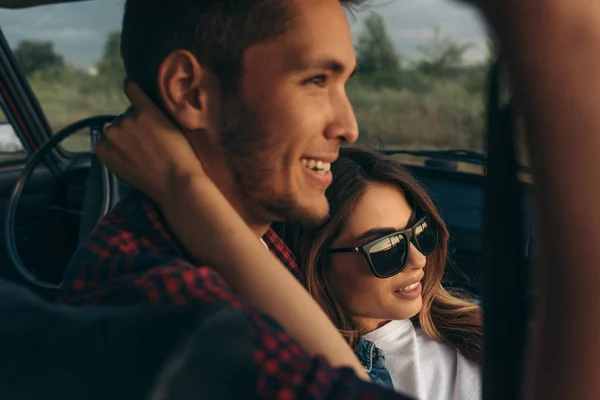 Close up portrait of romantic young couple going on a long drive in car on sunset light. Handsome young woman wearing sunglasses with handsome boyfriend on a road trip. Lifestyle concept. — Stock Photo, Image