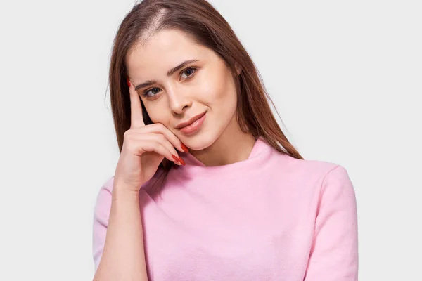 Pensive całkiem piękna młoda kobieta nosi różowy t-shirt, wygląda przyjemnie do aparatu, stawia przed białym tle Studio. Koncepcja ludzi emocji — Zdjęcie stockowe