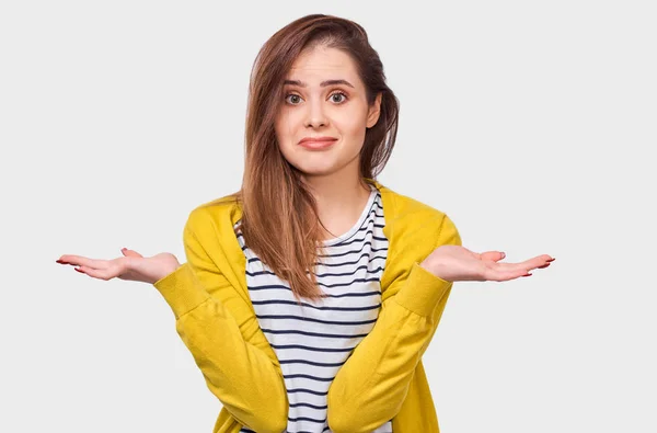 Ondervraagd jonge vrouw, onzeker tijdens het bespreken, gekleed in gestreepte t-shirt en gele Cardigan, poseren over witte muur. Student meisje heeft verward expressie. Mensen emoties — Stockfoto