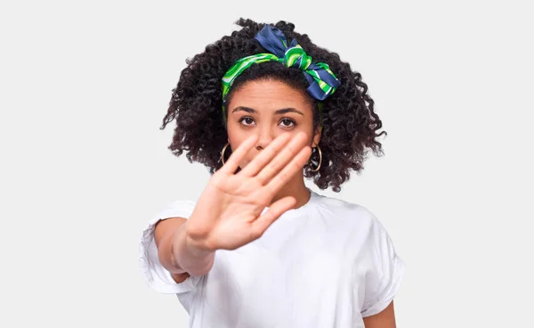 Афроамериканець молода жінка жести стоп знак з долоні, носити білу футболку і зелений заставку, позує проти білої стіни студії. Плутати жінки кажучи: ні!. Людей і емоцій — стокове фото