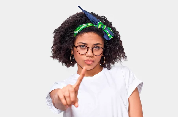 Афроамериканець молода жінка, одягнена в білу футболку і зелену заставку, вказує безпосередньо на камеру з вказівним пальцями, ізольовані над білою стіною. — стокове фото