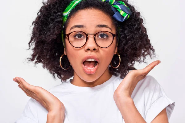 El retrato de cerca de la joven afroamericana conmocionada ha sorprendido la expresión. Hermosa hembra Afro oye algo increíble, mantiene las manos abiertas, aisladas sobre fondo blanco. Concepto de emociones — Foto de Stock