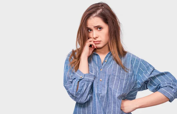 Pensive młoda kobieta ubrana w Denim Blue shirt, z palcem złożonym na ustach frown twarz i patrząc do aparatu na białym tle Studio. Przemyślany kobiece myślenie o czymś. — Zdjęcie stockowe