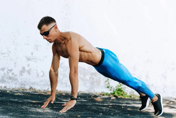 Strong fitness man doing exercise for chest outdoors against concrete wall. Copy space for advertising. Sportsman doing pushups workout outside. — Stock Photo, Image
