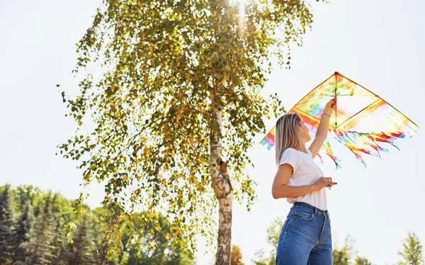 Imagem ao ar livre da jovem mulher feliz está lançando um papagaio em um dia ensolarado no verão. Bela fêmea brincando e se divertir fora com um papagaio no parque . — Fotografia de Stock