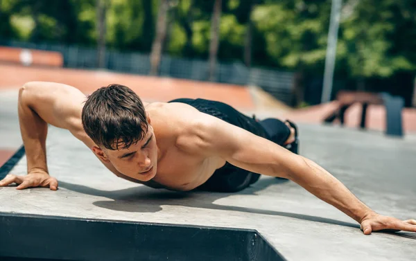 Athlete man doing push-ups on workout ground. Caucasian fitness male doing workout exercises on sunset light background. People and sport concept — Stock Photo, Image