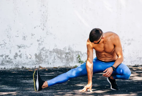 Image of jogger man stretching before exercises outdoors against concrete wall. Athlete male stretches after workout outside. Sport and people concept. Copy space for your text — Stock Photo, Image