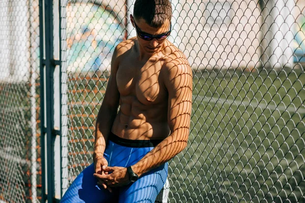 Imagem ao ar livre de um jovem atleta posando e olhando para um lado, descansando após o treino. O desportista inclinou-se contra a rede após o treino. Esporte e estilo de vida conceito — Fotografia de Stock