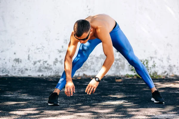 Sportsman s'étirant avant les exercices à l'extérieur contre un mur en béton. Athlète mâle s'étend après l'entraînement à l'extérieur. Concept de sport et de personnes. Copiez l'espace pour votre texte — Photo