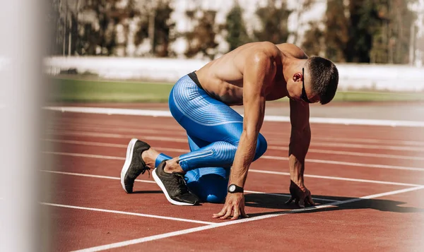 Fit shirtless man preparing for running on racetrack at stadium. Sportsman, male runner sprinting during training session for competition. People, sport and healthy lifestyle — Stock Photo, Image