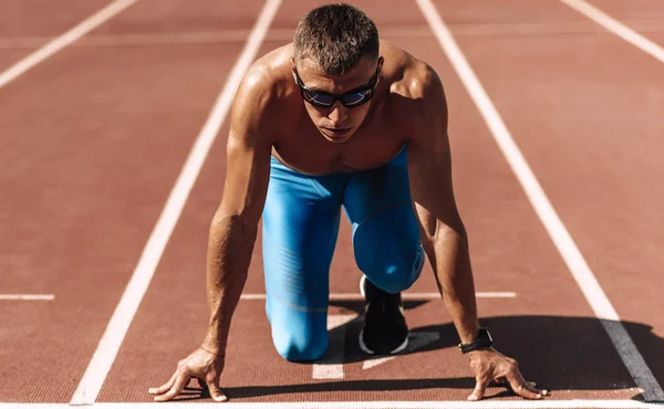 Image rapprochée d'un athlète se préparant à courir sur un hippodrome au stade. Sportsman, sprint de coureur masculin pendant la séance d'entraînement pour la compétition. Personnes, sport et mode de vie sain — Photo