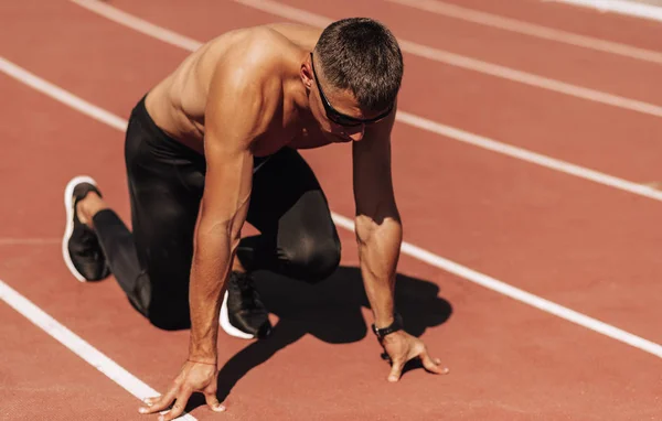 Stadyumda yarış pistinde koşmaya hazırlanan gömleksiz sporcu. Yarışma için eğitim oturumu sırasında erkek koşucu sprint. İnsanlar, spor ve sağlıklı yaşam tarzı — Stok fotoğraf