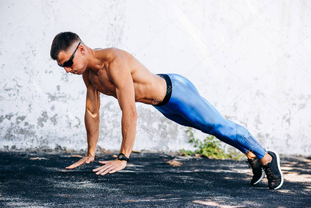Side view image of strong fit man doing exercise for chest outdoors against concrete wall. Copy space for advertising. Sportsman doing pushups workout outside.