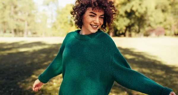 Imagem horizontal da bela jovem mulher sorrindo posando contra o fundo da natureza com cabelo encaracolado ventoso, tem expressão positiva, vestindo em suéter verde. Pessoas, viagens e conceito de estilo de vida . — Fotografia de Stock