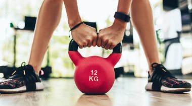 Spor salonunda ya da fitness kulübünde spor yaparken kırmızı bir kettlebell ile salıncak egzersizi yapan genç fitness kadınının yakın plan görüntüsü. Su ısıtıcılı güzel bacaklar..