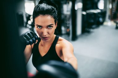 Genç kadın boksörün bir boks stüdyosunda büyük bir kum torbasına vurduğu yakın plan görüntüsü. Sporcu kadın boksör spor salonunda sıkı çalışıyor. Spor, yaşam tarzı ve insanlar konsepti.