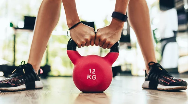 Cropped close-up image of young fitness woman doing swing exercise with a red kettlebell as a part of a fitness workout in the gym or fitness club. Beautiful legs with kettle bell. — Stock Photo, Image