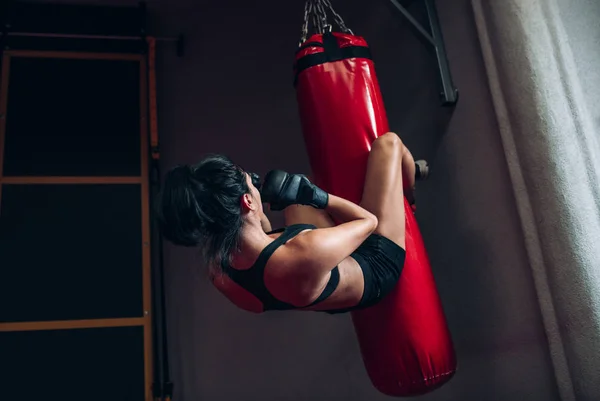 Imagen de vista trasera de una joven boxeadora golpeando un enorme saco de boxeo en un estudio de boxeo. Deportiva kickboxer entrenando duro en el gimnasio. Concepto de deporte, estilo de vida y personas . — Foto de Stock