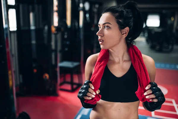 Strong brunette woman with red towel on neck before workout with punch bag, wearing kickboxing gloves in the gym. Sport, fitness, lifestyle and people concept. — Stock Photo, Image